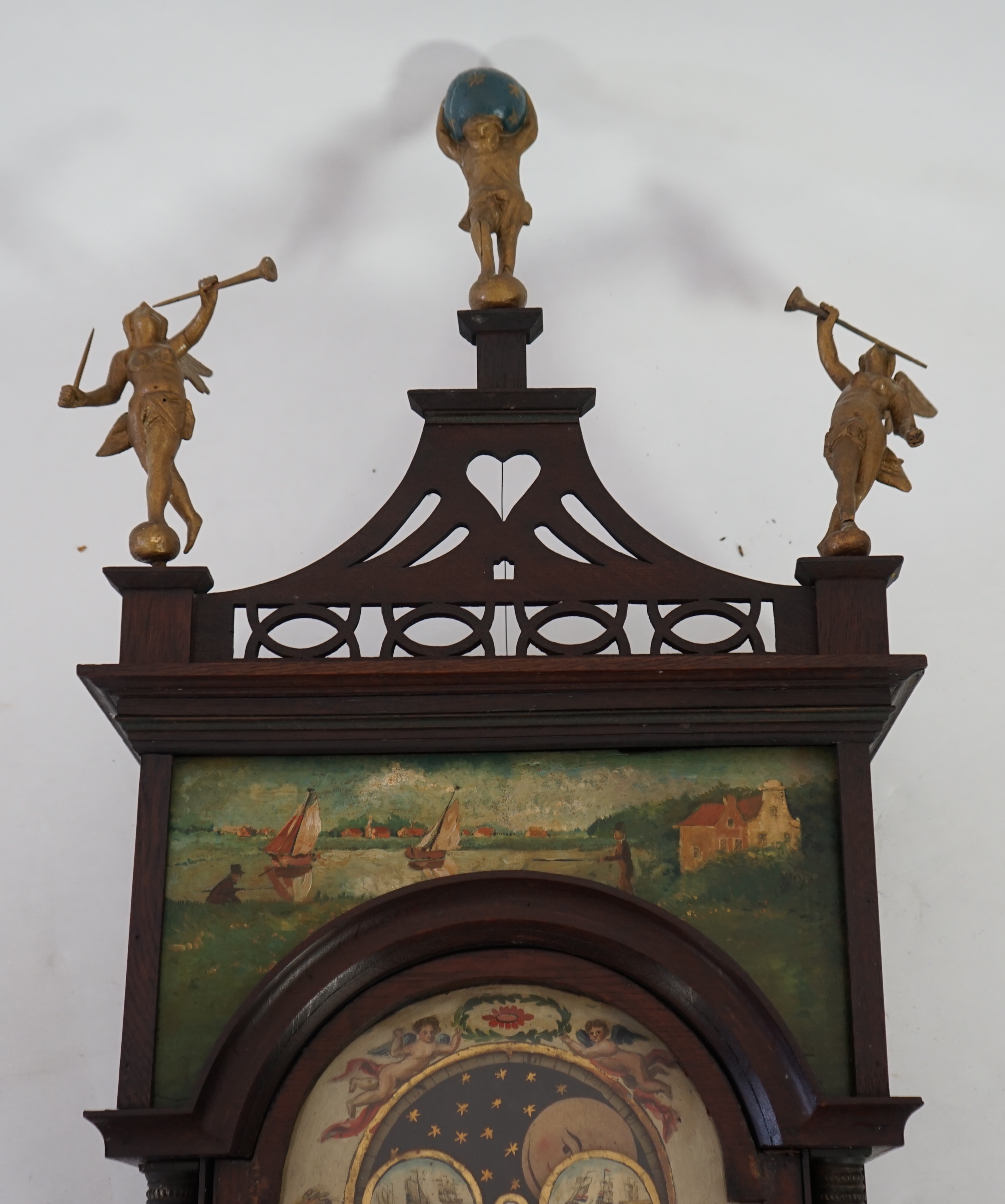A late 18th century Dutch Frisian Staart oak eight day wall clock, with atlas and angel finials, hood painted with a Dutch riverscape and painted arched dial with moonphase, date aperture and alarm indicator, 47cm wide,